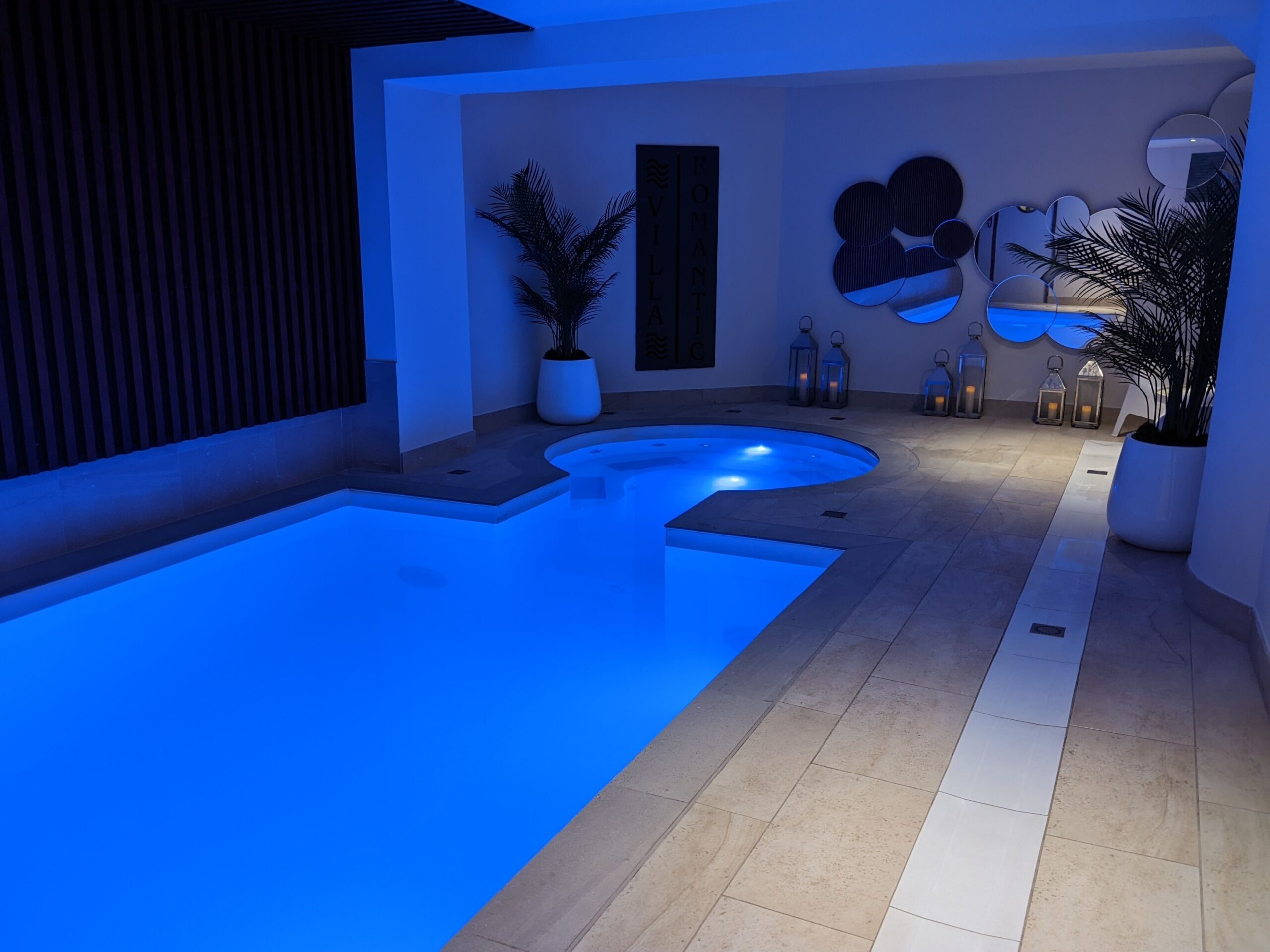 Long rectangular pool with jacuzzi at one end and chairs to sit in on the outside