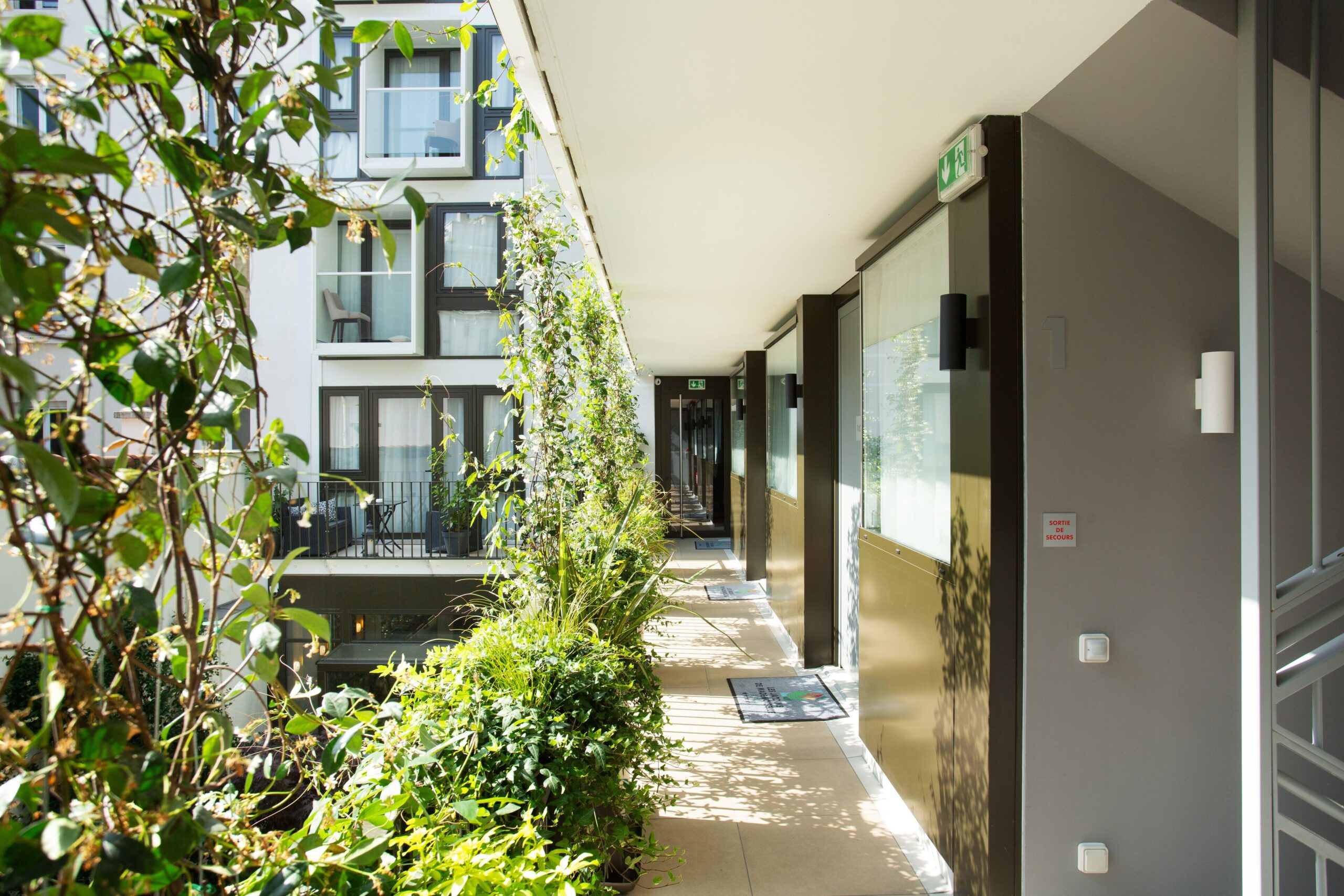 Outdoor corridor on the top floor, with plants hanging from the railing, room balconies can be seen at the distance